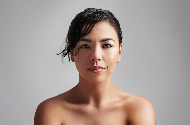 Foto de estudio naturalmente impecable de una mujer joven con el pelo mojado posando sobre un fondo gris