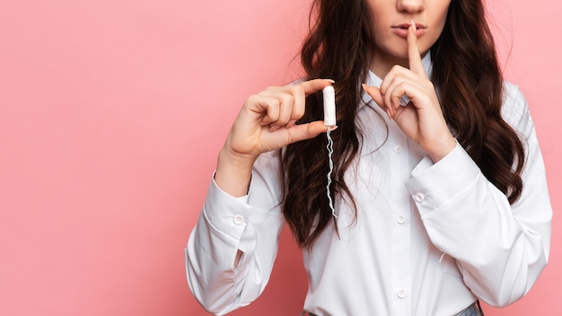 Una foto de estudio de una niña sosteniendo un tampón en la mano en un aplicador menstrual. Espacio para el texto. El concepto de higiene femenina.