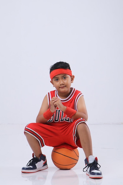 Foto de estudio de un niño asiático con una camiseta roja sosteniendo una pelota de baloncesto