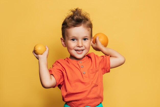 Foto de estudio de un niño sonriente sosteniendo un limón fresco y una naranja sobre un fondo amarillo El concepto de alimentos saludables para bebés con vitamina C