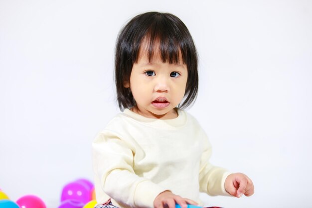 Una foto de estudio de una pequeña y linda modelo asiática de pelo negro corto con una falda a cuadros informal sentada en el suelo sonriendo riendo jugando con un colorido juguete de bolas redondas solo en un fondo blanco.