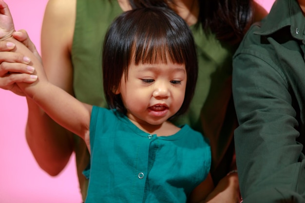 Foto de estudio de primer plano de la joven madre asiática feliz padre de la familia y la pequeña hija linda sentada en el suelo juntos sonriendo miran la cámara sosteniendo globos de colores sobre fondo rosa.