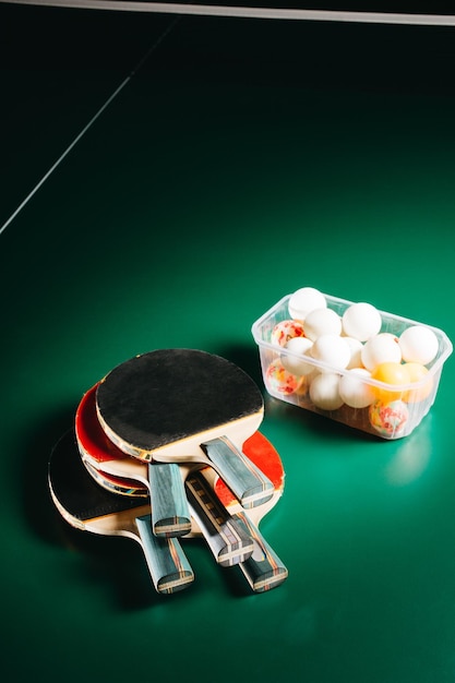 Foto de estudio de raquetas de ping pong y caja de pelotas en la mesa de juego verde
