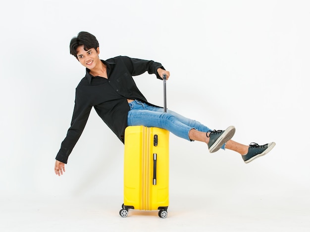 Foto foto de estudio de retrato de un joven asiático lgbt gay bisexual homosexual modelo de viajero masculino con camisa negra casual y jeans de mezclilla sentado sonriendo en el equipaje del carrito posando mirando a la cámara sobre fondo blanco