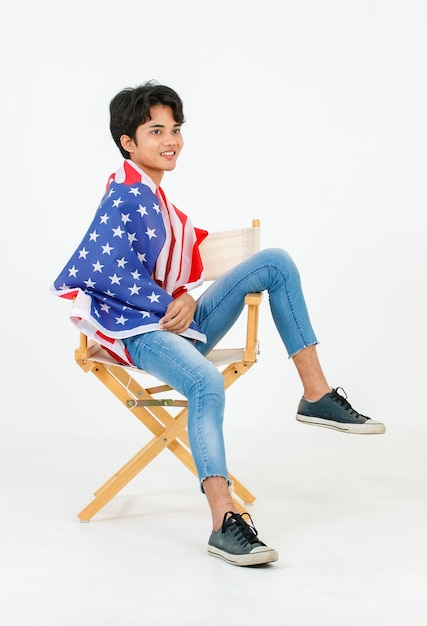 Foto de estudio de retrato de un joven asiático LGBT gay bisexual homosexual en topless modelo de moda masculino sentado en una silla sonriendo usando el cuerpo de la cubierta de la bandera nacional de los Estados Unidos de América sobre fondo blanco