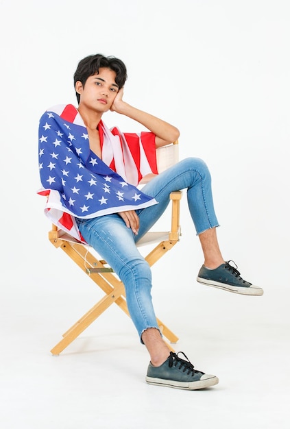 Foto de estudio de retrato de un joven asiático LGBT gay bisexual homosexual en topless modelo de moda masculino sentado en una silla sonriendo usando el cuerpo de la cubierta de la bandera nacional de los Estados Unidos de América sobre fondo blanco