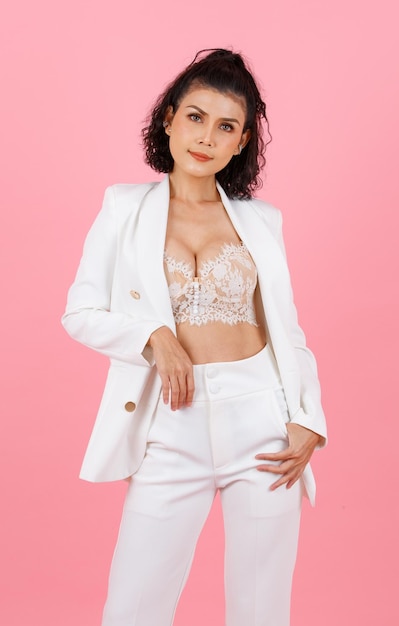 Foto de estudio de retrato de mujer de negocios exitosa profesional de peinado rizado asiático sexy en traje casual de moda blanco con sujetador de lencería de encaje de pie mirando a la cámara sobre fondo rosa