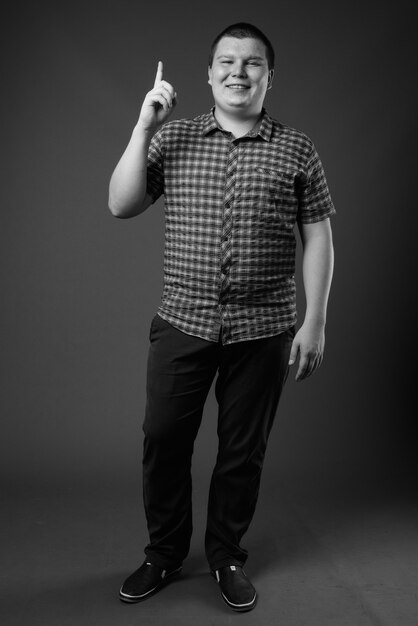 Foto de estudio de sobrepeso joven vistiendo camisa a cuadros púrpura contra la pared gris