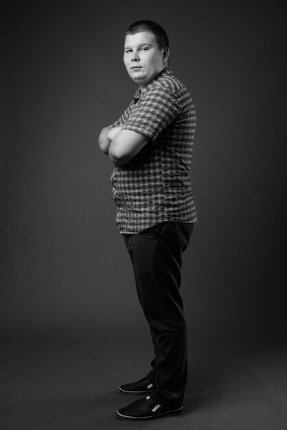 Foto de estudio de sobrepeso joven vistiendo camisa a cuadros púrpura contra la pared gris