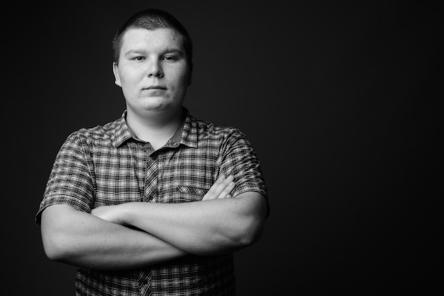 Foto de estudio de sobrepeso joven vistiendo camisa a cuadros púrpura contra la pared gris