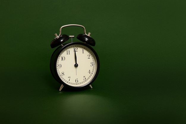 Foto de estudio con sombras suaves de un reloj de alarma negro con medianoche en la esfera del reloj aislado sobre fondo verde oscuro con espacio para copiar anuncios. Es hora de celebrar la Navidad y el Año Nuevo.