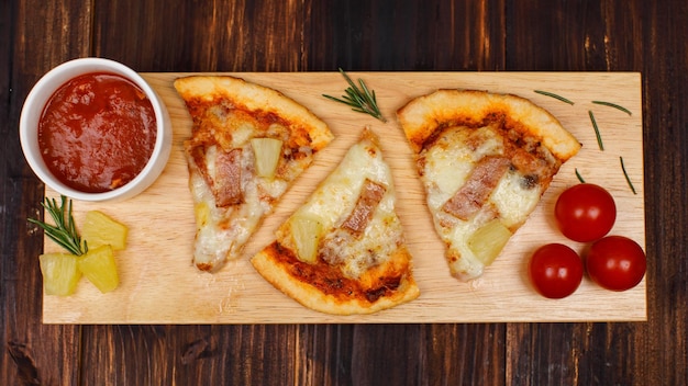 Foto de estudio de vista superior de primer plano de tres piezas de horno caliente horneado sabroso delicioso jamón casero italiano y pizza de corteza de pan suave hawaiano de piña decorada en una placa de madera con salsa de tomate