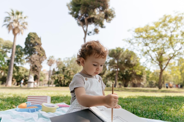 Foto exterior de una linda y encantadora niña con rizos vistiendo ropa de verano sentada en el parque