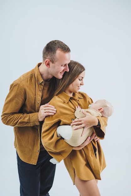 Foto de familia casera sobre un fondo blanco de padres felices con un bebé recién nacido durmiendo en sus brazos Una madre y un padre felices tienen a su hijo de 4 meses en sus brazos