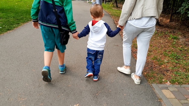 Foto de familia feliz con niño pequeño sosteniendo por las manos y caminando en el parque