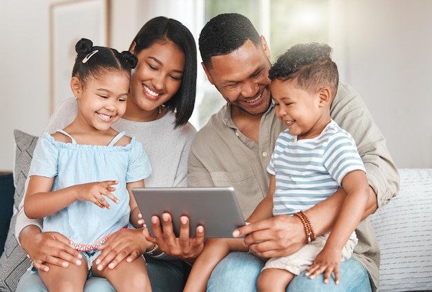 Una foto de una familia joven que se une felizmente mientras usa una tableta digital en el sofá de casa