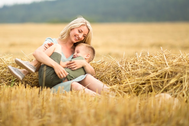 Foto de familia: mamá rubia con cabello largo e hijo jugando en el campo