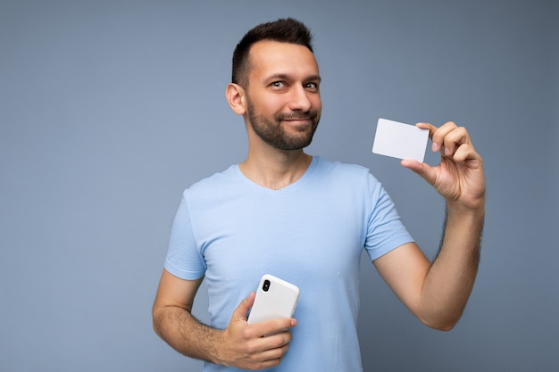 Foto de feliz apuesto joven brunet sin afeitar con barba vistiendo camiseta azul todos los días aislado