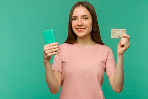 Foto de feliz contento gritando joven posando aislado sobre fondo de pared azul mediante teléfono móvil con tarjeta de crédito.