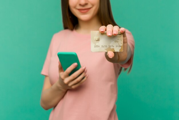 Foto de feliz contento gritando joven posando aislado sobre fondo de pared azul mediante teléfono móvil con tarjeta de crédito.