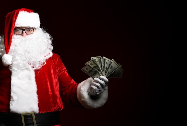 Foto de feliz Santa Claus con billetes de un dólar mirando a la cámara sobre fondo negro