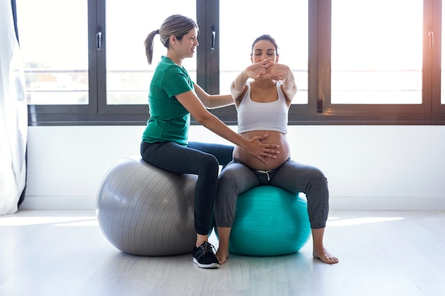 Foto de fisioterapeuta ayudando a hermosa mujer embarazada para hacer ejercicios de pilates con pelota preparándose para el parto.