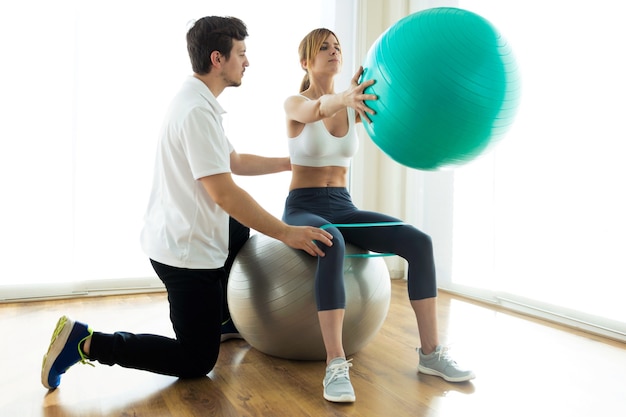 Foto foto de fisioterapeuta que ayuda al paciente a hacer ejercicio en la pelota de fitness en la sala de fisioterapia.