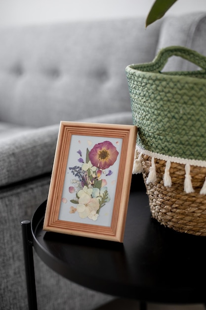 Una foto de flores secas en un marco de madera en el interior de una mesa cerca de un sofá gris y una casa