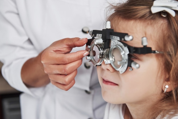 Foto focada de criança em foróptero tendo testando seus olhos no consultório médico.