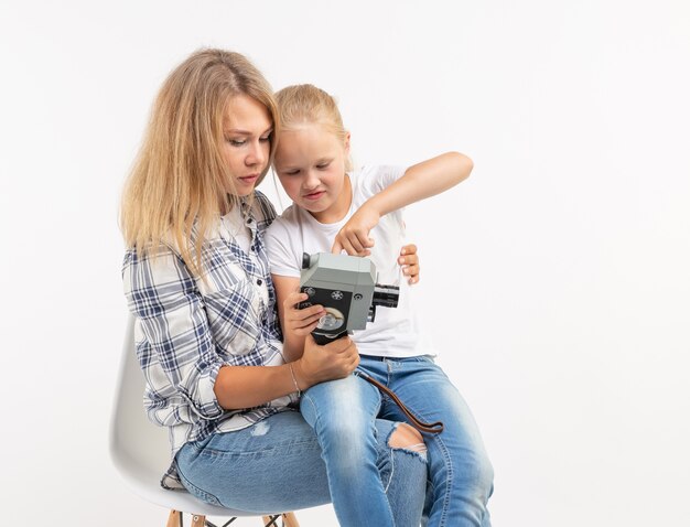 Foto foto, fotógrafo e conceito de câmera retro - jovem e sua filha adolescente usando uma câmera vintage em fundo branco.