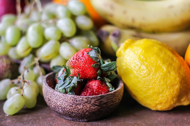 Foto de fresas frescas con la hoja de fresa sobre fondo gris rústico. Un montón de fresas maduras sobre la mesa con limón uva kiwi plátano. Copia espacio Alimentos orgánicos. Comida clara