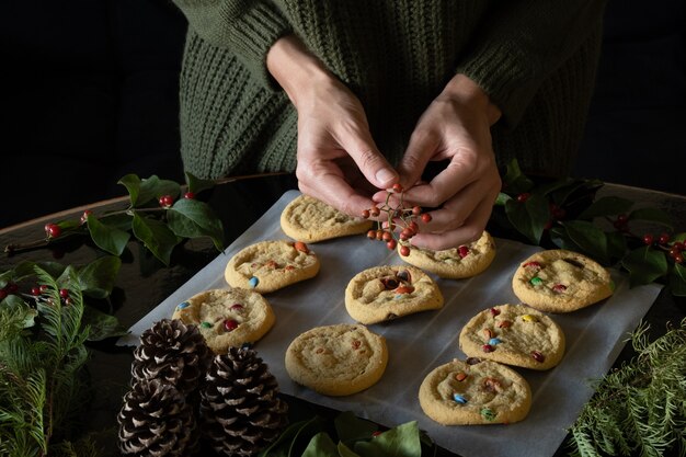 Foto frontal de uma mulher irreconhecível decorando biscoitos de natal, fundo escuro, estilo escuro