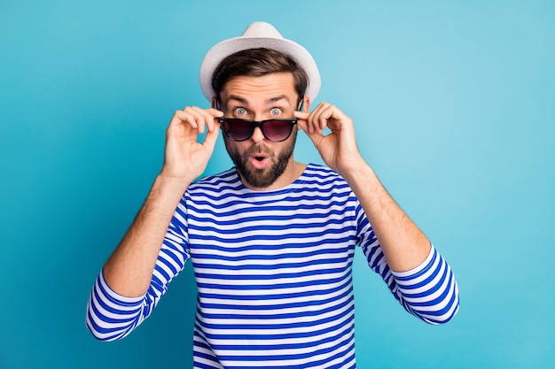 Foto de funky emocionado guapo turista despegando fresco sol negro especificaciones boca abierta leer descuentos banner desgaste camisa de marinero a rayas gorra color azul aislado