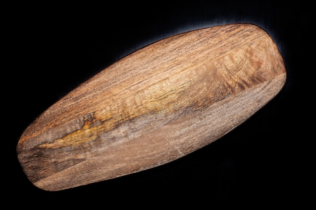 Foto genérica de una tabla de madera ovalada natural sobre un fondo negro.