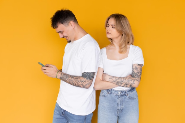 Foto de gente emocionada positiva, hombre y mujer usando teléfonos móviles aislados sobre amarillo