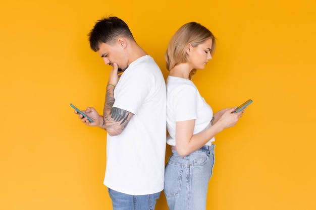 Foto de gente emocionada positiva, hombre y mujer usando teléfonos móviles aislados sobre amarillo