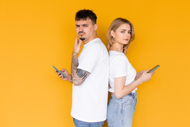 Foto de gente emocionada positiva, hombre y mujer usando teléfonos móviles aislados sobre amarillo