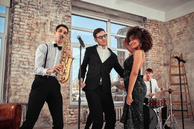 Foto de un grupo musical étnico en estudio. Músicos y una solista afroamericana posando en cámara, durante un ensayo, fondo loft.