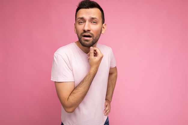 Foto foto de guapo pidiendo insatisfecho hombre brunet dudoso en camiseta rosa casual aislado en rosa