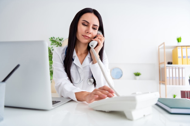 Foto de la hermosa doctora seria usar netbook en la mesa hablando por teléfono