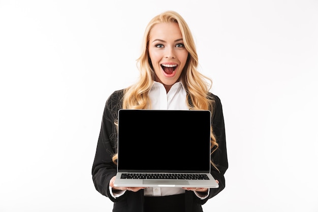 Foto de hermosa empresaria vistiendo traje de oficina sonriendo mientras sostiene el portátil con pantalla negra, aislado