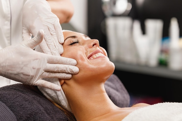 Una foto de una hermosa joven disfrutando de un masaje facial en el salón de belleza.