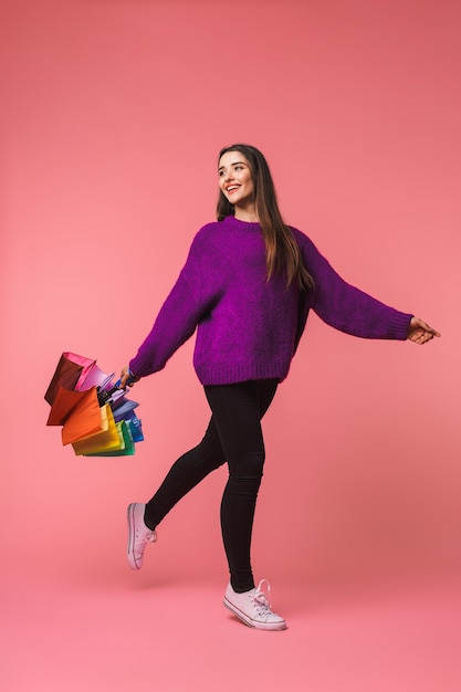 Foto de una hermosa joven emocional posando aislada sobre espacio rosa sosteniendo paraguas arco iris.