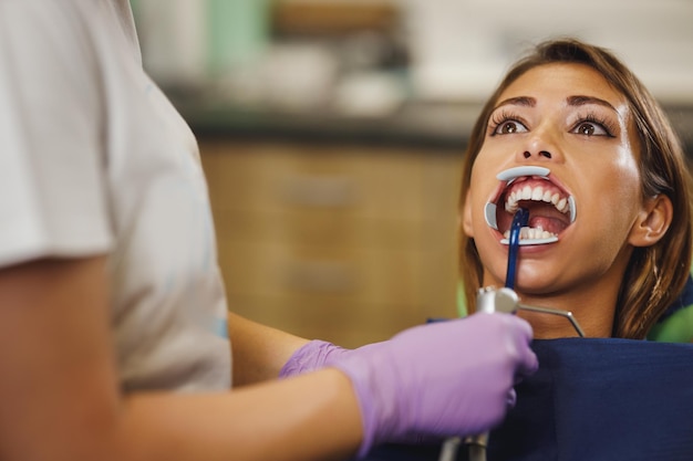 La foto de una hermosa joven está en el dentista. Ella se sienta en la silla del dentista y el dentista se prepara para colocar aparatos ortopédicos en sus dientes y colocar bloqueos linguales autoalineables estéticos.
