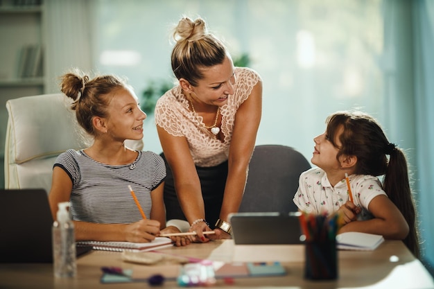 Foto de una hermosa joven madre ayudando a sus dos hijas con la tarea durante la pandemia de COVID-19.