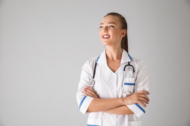 Foto de una hermosa joven médico cosmetólogo aislado sobre pared gris.