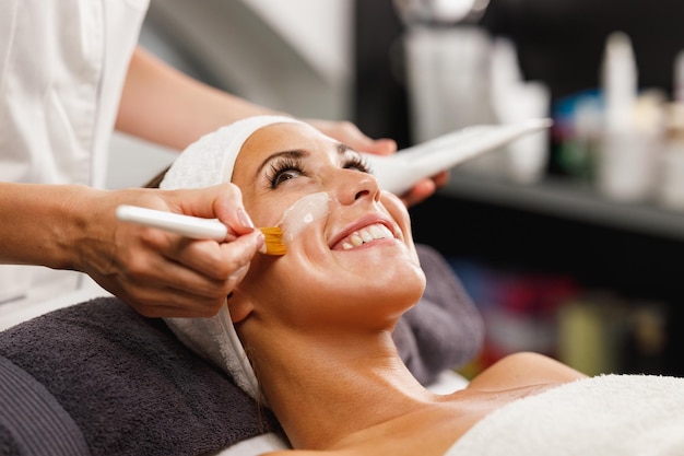 Foto de una hermosa joven recibiendo un tratamiento de máscara facial en el salón de belleza.