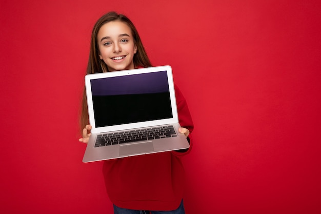 Foto foto de la hermosa joven sosteniendo la computadora portátil aislada sobre la pared colorida.