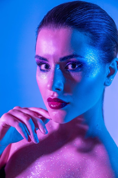 Foto de hermosa modelo morena en el estudio con filtros de color Resplandor de belleza de moda Cara de primer plano de una hermosa mujer brunete en luz de neón púrpura y azul