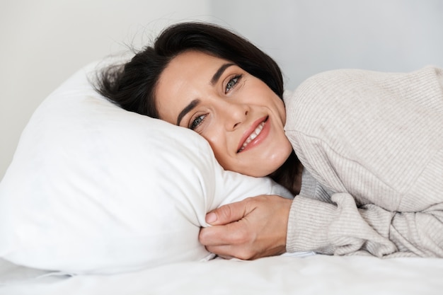 Foto de hermosa mujer de 30 años acostada en la cama, sobre una almohada blanca en casa